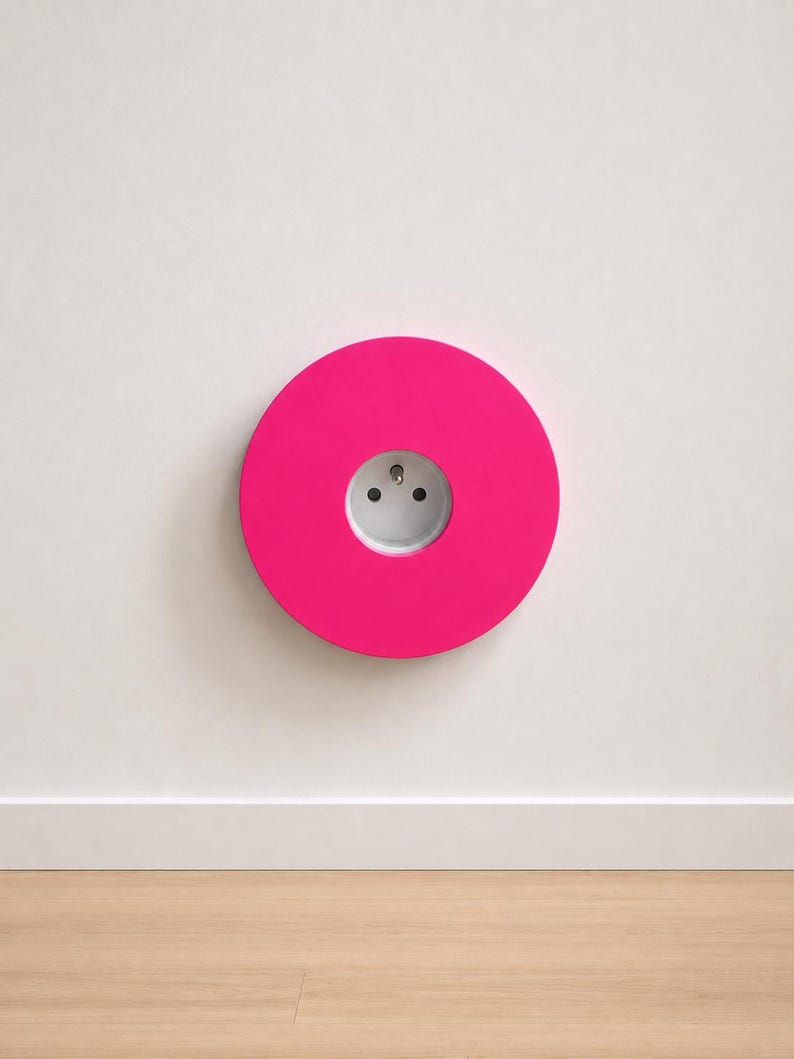 K&ouml;nnte beinhalten: Eine kreisf&ouml;rmige, leuchtend pinke Wandplatte mit einer mittig platzierten wei&szlig;en Steckdose. Das Design ist flach und geometrisch, mit einer glatten, einfarbigen Oberfl&auml;che, die die standardm&auml;&szlig;ige runde Steckdose in der Mitte umschlie&szlig;t.
