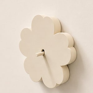 以下が含まれることがあります： 5枚の花びらを持つ花のような形をしたクリーム色のウォールフック。滑らかでマットな質感で、花の中央から円筒形のペグが突き出しており、平らな壁面に取り付けられるように設計されています。