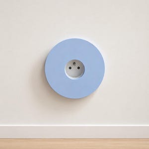 K&ouml;nnte beinhalten: Eine kreisf&ouml;rmige, hellblaue Wandplatte mit einer mittig platzierten Steckdose. Die Platte hat eine glatte, matte Oberfl&auml;che und einen vertieften kreisf&ouml;rmigen Bereich, der die wei&szlig;e Standard-Steckdose mit dunkelgrauen Details umgibt.