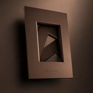 May include: A rectangular dark brown frame with a smooth matte finish. The frame features a central opening with layered geometric shapes visible inside. The text "MADE IN ITALY" is embossed in small capital letters at the bottom of the frame.