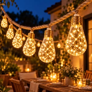 Pode incluir: Uma corrente de luzes para exterior com lâmpadas de vidro transparente suspensas por uma corda grossa de cor natural. Cada lâmpada contém um conjunto de luzes quentes, criando um efeito brilhante ao longo do cabo.