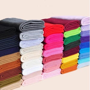 Puede incluir: Una colección de muestras de tela acanalada dobladas dispuestas en varias pilas verticales. Las piezas de tela muestran un amplio espectro de colores, incluidos tonos negros, grises, rojos, rosas, verdes, azules, amarillos, naranjas, marrones y blancos.