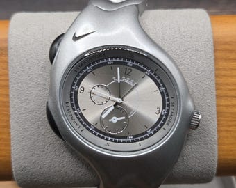 Reloj Nike Triax con esfera plateada, diseño futurista Y2K y caja de regalo metálica.