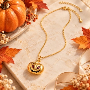 Pode incluir: Um colar de tom dourado com um pingente de abóbora de Halloween que possui dois pequenos olhos de pedra preciosa vermelha. O pingente pende de uma delicada corrente dourada que inclui um extensor ajustável com um pequeno pingente em gota.