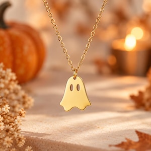 Op de afbeelding: Een goudkleurige ketting met een platte, gepolijste hanger in de vorm van een geest met twee ovale uitsparingen voor de ogen. De hanger hangt aan een fijne, dunne goudkleurige ketting met kleine, uniforme ronde schakels voor een strak ontwerp.