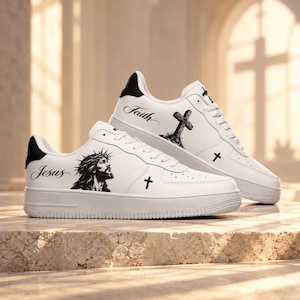 May include: A pair of white sneakers with black accents featuring a graphic of Jesus wearing a crown of thorns on one shoe and a cross with the word Faith on the other. Both shoes include small black cross symbols and white laces.