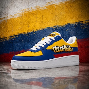 Op de afbeelding: Een lage sneaker met een geel, blauw en rood kleurenschema geïnspireerd op de Colombiaanse vlag. Het zijpaneel toont het woord COLOMBIA in een gestileerd graffitilettertype, aangevuld met witte veters en een effen witte rubberen zool.