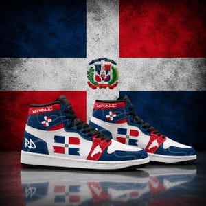 Può includere: Sneakers alte con una combinazione di colori blu, bianco e rosso ispirata alla bandiera della Repubblica Dominicana. Le scarpe presentano la scritta "REPUBLIC" sul colletto, "RD" sul tallone e piccole icone di bandiere sui lati e sulla punta.