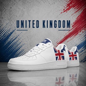 Può includere: Un paio di sneakers bianche con un design della bandiera Union Jack sul tallone e sui pannelli laterali. Le scarpe hanno lacci bianchi, una suola bianca e il testo UNITED KINGDOM stampato in blu scuro sopra le sneakers su sfondo strutturato.
