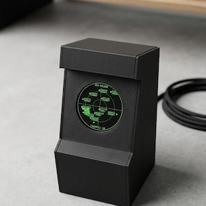 Op de afbeelding: Een matzwart, rechtopstaand elektronisch apparaat met een rond scherm dat een groene radarinterface weergeeft. Het scherm toont de tekst RIX RADAR en TRAFFIC: 18, samen met diverse alfanumerieke codes en cirkelvormige rasterlijnen.