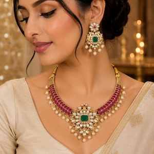 May include: A gold-toned necklace and matching earring set featuring rectangular magenta stones, a central square green stone, and white pearl accents. The necklace has a structured band with a floral-inspired pendant and dangling pearls.