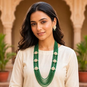 May include: A multi-strand necklace featuring small green beads arranged in several layers, accented by six gold-toned, star-shaped floral motifs with white stones. Matching star-shaped earrings with green bead drops complete the set.