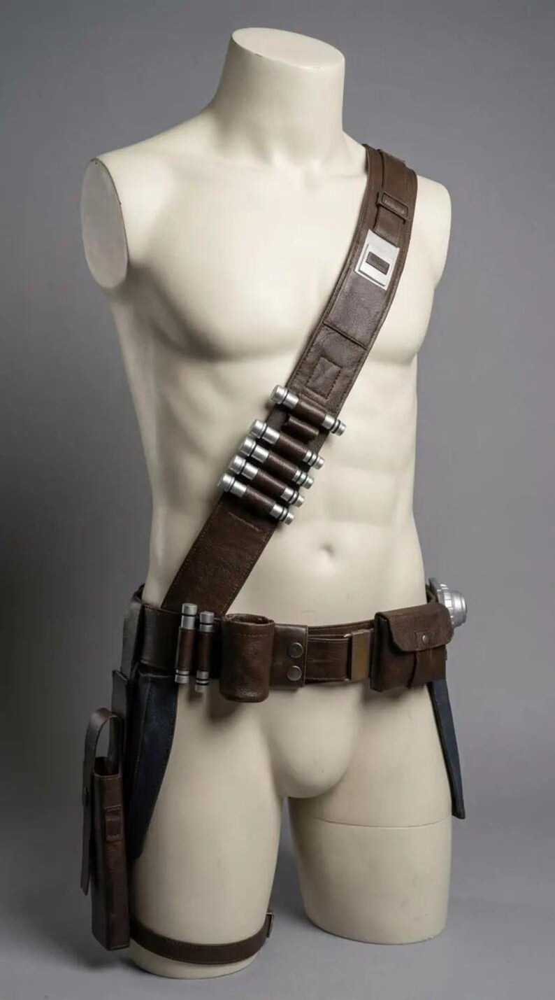 May include: A brown leather utility belt and shoulder strap set featuring silver-colored cylindrical canisters attached to the chest band. The gear includes a waist belt with multiple pouches, a holster, and a metallic buckle, worn on a mannequin.