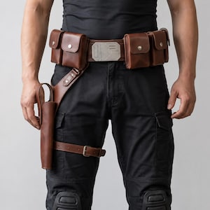 May include: A brown leather utility belt featuring four rectangular pouches with metallic snap closures, a central rectangular silver-toned buckle with engraved line details, and an attached drop-leg holster with a buckled thigh strap.