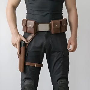 May include: A brown leather utility belt featuring four rectangular pouches with metal snap closures, a central metallic buckle plate, and an integrated drop-leg holster with a buckled thigh strap, worn over black tactical trousers and a black shirt.