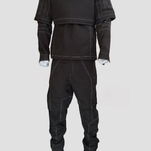 Peut inclure: Un ensemble compos&eacute; d'une chemise &agrave; manches longues et d'un pantalon marron fonc&eacute;, dot&eacute; d'un col montant et d'un panneau de poitrine superpos&eacute;. Le v&ecirc;tement est rehauss&eacute; de surpiq&ucirc;res blanches visibles sur les manches, le torse et les jambes.