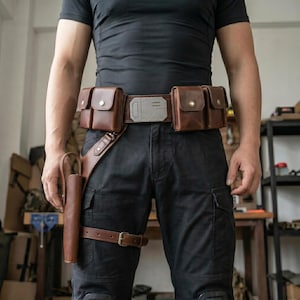 May include: A brown leather utility belt featuring two rectangular pouches on each side, a central metallic buckle with geometric detailing, and a matching leather holster attached to the right side with a leg strap, worn over black pants.
