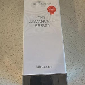 May include: A rectangular white SkinMedica TNS Advanced+ Serum box with a silver metallic base. The front features the brand logo, product name, and a red Allure Best of Beauty Hall of Fame seal. The net weight is clearly printed as 1.0 oz. / 28.4 g.