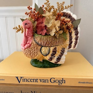 Peut inclure: Un cache-pot en céramique en forme de dinde avec un corps texturé brun et beige, une tête et un cou roses. Le cache-pot est rempli d'un arrangement de baies orange séchées, de feuilles vertes et de fleurs d'hortensia roses et crème.