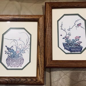 Puede incluir: Dos láminas enmarcadas con ilustraciones botánicas y de aves. Cada lámina está en un marco de madera de tono medio con un paspartú color crema y un borde octogonal verde oscuro. Las obras representan pájaros sobre ramas florecidas en macetas.