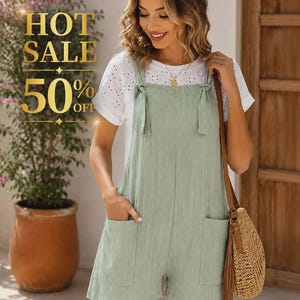 Puede incluir: Un romper sin mangas en color verde salvia con tirantes anudados y dos bolsillos delanteros, usado sobre una blusa blanca de manga corta con bordado inglés. El romper tiene un corte corto y un acabado de tela texturizada.
