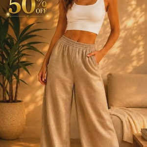 Può includere: Una canotta bianca a coste abbinata a pantaloni della tuta beige dal taglio ampio con elastico in vita e tasche laterali. L'immagine include un testo dorato che recita HOT SALE 50% OFF. L'outfit è completato da scarpe da ginnastica bianche.
