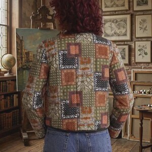 Peut inclure: Une veste &agrave; manches longues pr&eacute;sentant un motif patchwork compos&eacute; de paisley et de bandana dans des tons vert olive, orange br&ucirc;l&eacute; et noir. La veste a un ourlet droit et est port&eacute;e avec un jean bleu. Le v&ecirc;tement est vu de dos.