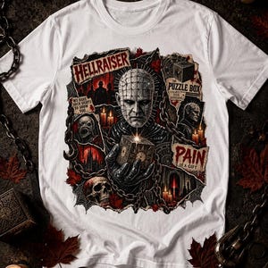 May include: A white t-shirt featuring a graphic print of the Hellraiser character Pinhead holding a puzzle box. The design includes text that reads HELLRAISER, THE PUZZLE BOX, WE HAVE SUCH SIGHTS TO SHOW YOU, and PAIN IS A GIFT, surrounded by chains.