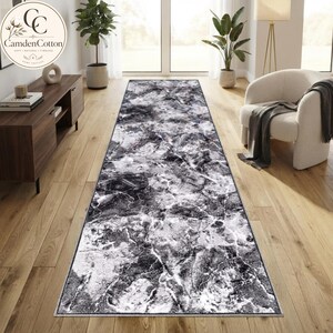 May include: A long rectangular runner rug featuring a high-contrast black and white marble-inspired pattern with intricate veining throughout. The rug has a low-profile texture and is positioned centrally on a light-coloured wooden floor surface.