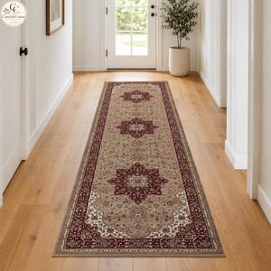 May include: A long rectangular runner rug featuring a beige background with a repeating pattern of dark red and cream-coloured floral medallions. The rug has a wide, ornate border in dark red and cream, showcasing intricate, symmetrical designs.