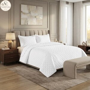May include: A white bedspread with a diamond-stitched quilted pattern covering a bed with two matching pillows. The bedding set features a clean, uniform texture and bright white colour, providing a neutral look for a bedroom space.