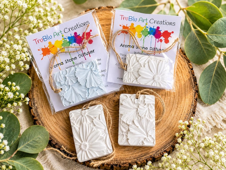 May include: Four rectangular aroma stone diffusers with embossed floral patterns. Two are packaged in clear plastic with cards labeled TruBlu Art Creations Aroma Stone Diffuser, while two are loose. All feature attached jute twine hanging loops.