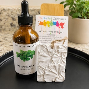 May include: A brown glass bottle of Brooklyn Botany Peppermint Essential Oil with a black dropper cap, next to a white rectangular plaster aroma stone diffuser with a floral relief pattern and a TruBlu Art Creations instruction card.
