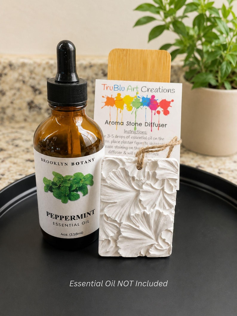 May include: A brown glass bottle of Brooklyn Botany Peppermint Essential Oil with a black dropper cap, next to a white rectangular plaster aroma stone diffuser with a floral relief pattern and a TruBlu Art Creations instruction card.