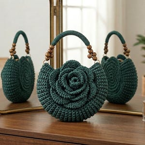 May include: A dark green crochet handbag featuring a prominent three-dimensional rose design on the front. The bag has a rounded shape and a single handle accented with small, round, brown wooden beads on both sides of the handle attachment points.