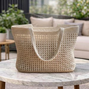 May include: A cream-coloured crochet tote bag featuring an open-weave grid pattern throughout the body, a solid base, and two integrated handles. The bag has a structured rectangular shape with a wide opening and a smooth, light-coloured interior lining.