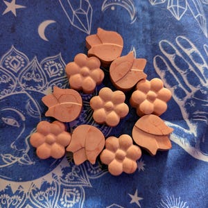 Peut inclure: Collection d'objets en forme de fleurs et de feuilles de couleur pêche disposés sur une surface bleue à motifs. Les formes de fleurs ont plusieurs pétales, tandis que les formes de feuilles ont un aspect texturé. Le fond présente des motifs célestes et géométriques.