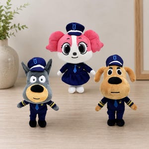 May include: Three plush toys dressed in blue uniforms with matching caps. The center figure has pink hair and a blue dress. The left figure is a gray animal with pointed ears, and the right figure is a tan animal with floppy ears.