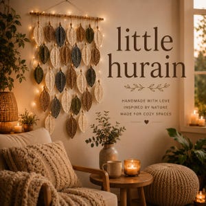May include: A wall hanging featuring multiple crocheted leaf shapes in shades of cream, brown, and dark green, suspended from a horizontal wooden rod with integrated string lights. The text little hurain is printed on the wall nearby.
