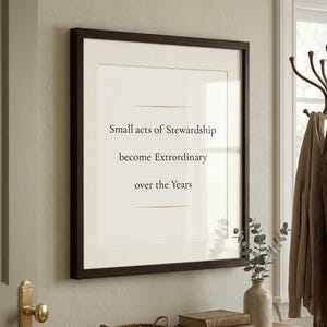 May include: A square wall art piece in a dark brown frame featuring a cream-colored background with black text that reads: Small acts of Stewardship become Extrordinary over the Years, accented by two thin horizontal lines above and below the text.
