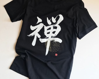 May include: Black t-shirt featuring a white Japanese kanji character "Zen" printed on the front. The character is styled with gold accents and a red seal.