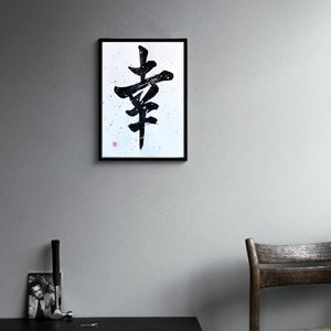 May include: Black and white calligraphy art print of the Japanese character for "happiness" framed in a black frame and hanging on a gray wall.