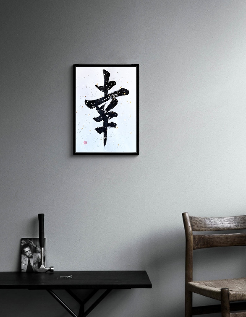 May include: Black and white calligraphy art print of the Japanese character for "happiness" framed in a black frame and hanging on a gray wall.