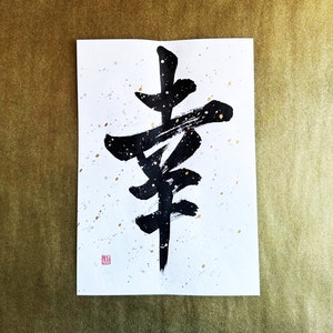 May include: Black ink calligraphy on white paper with gold speckles. The calligraphy depicts the Japanese character for "happiness".