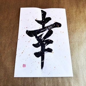 May include: Black ink calligraphy on white paper with gold speckles. The calligraphy depicts the Japanese character for "happiness".