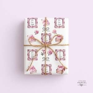 Pode incluir: Um presente retangular embrulhado em papel branco com um padrão repetitivo de livros cor-de-rosa, rosas cor-de-rosa e molduras cor-de-rosa ornamentadas contendo o texto One more chapter. O pacote está atado com um fio castanho fino.