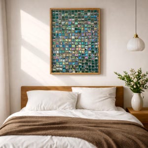 May include: A rectangular wall art piece featuring a grid of small, iridescent square tiles in shades of teal, blue, green, and purple, framed in light wood. The artwork is displayed above a bed with white pillows and a brown throw blanket.