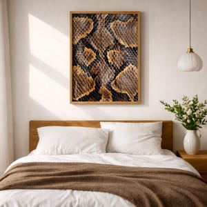 Könnte beinhalten: Ein rechteckiges Wandkunstwerk mit einem detaillierten, kontrastreichen Schlangenhautmuster in Braun-, Schwarz- und Beigetönen, gerahmt in einer hellen Holzleiste, platziert über einem Bett mit weißen Kissen und einer braunen Tagesdecke.