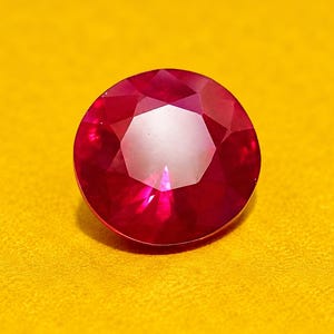 以下が含まれることがあります： 深く鮮やかな赤色をした、円形のファセットカットが施された宝石。この石は、光を反射する複数の三角形や凧形のファセットを持つブリリアントカットが特徴で、磨かれた表面全体に透明感のある輝きを放っています。