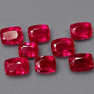 Puede incluir: Siete rubíes sueltos de talla cojín con un color rojo intenso y vibrante y superficies facetadas. Cada piedra preciosa muestra una forma rectangular con esquinas redondeadas, reflejando la luz a través de su parte superior pulida.